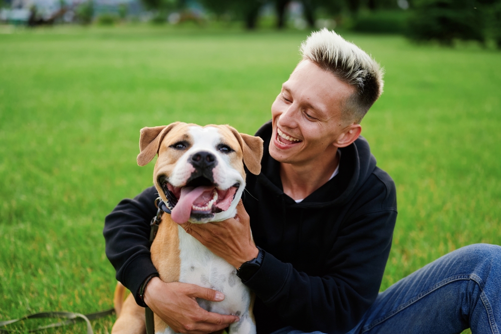 A joyful man and his playful dog share a happy moment sitting on the grass in a sunny park, radiating pure joy and connection. - veterinarian