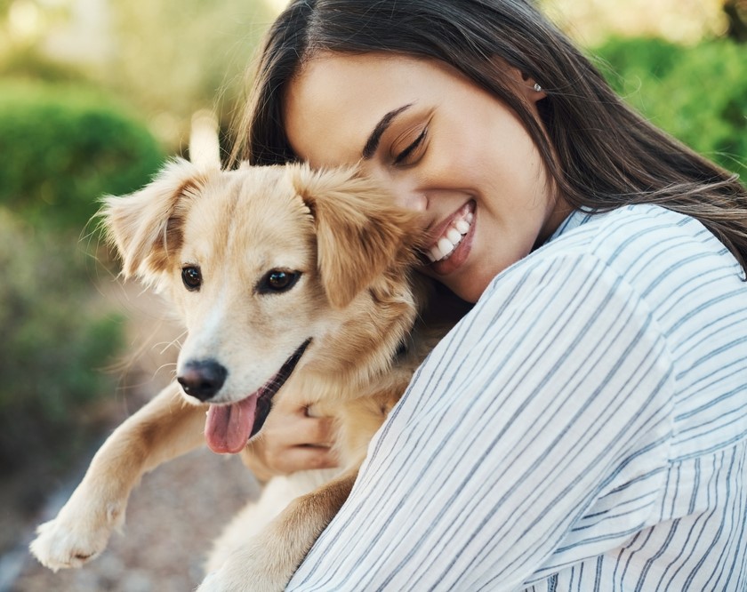 A woman smiling with her eyes closed, hugging a happy dog outdoors - veterinarian